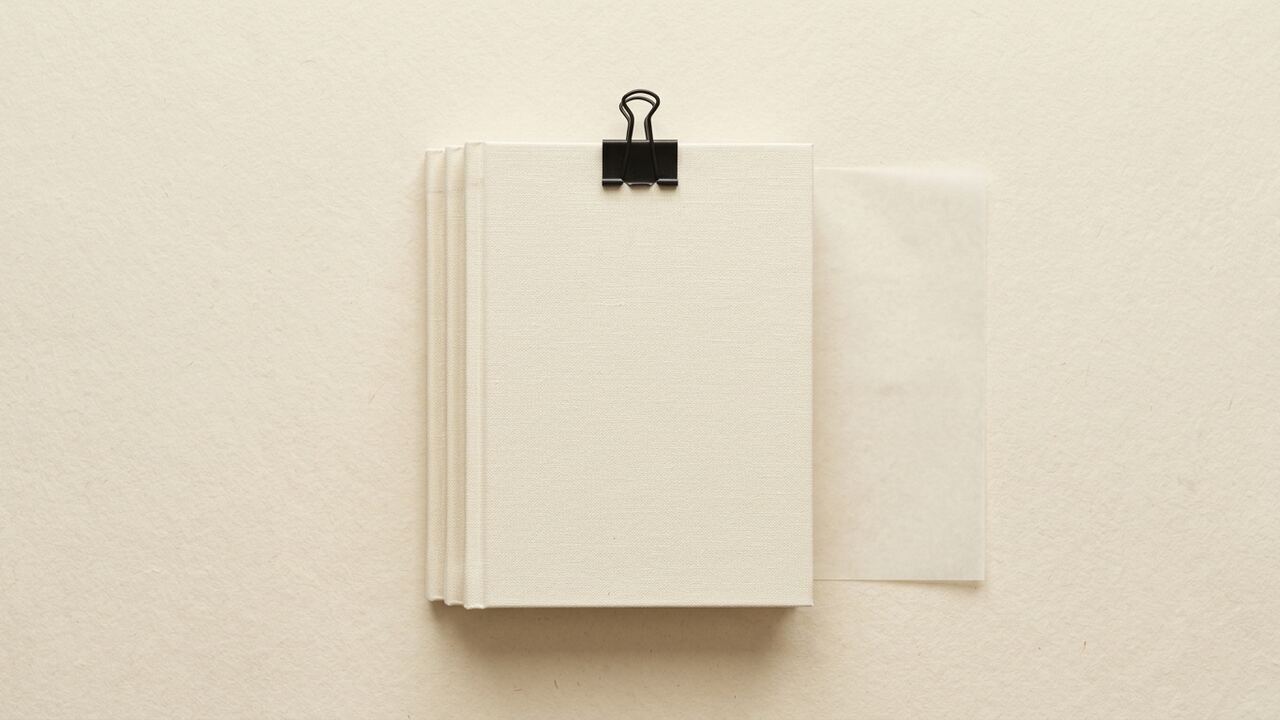 Illustrative brand image, synthetic: a squared stack of cream linen-bound folios held by a single binder clip, with one loose vellum sheet lying beside them